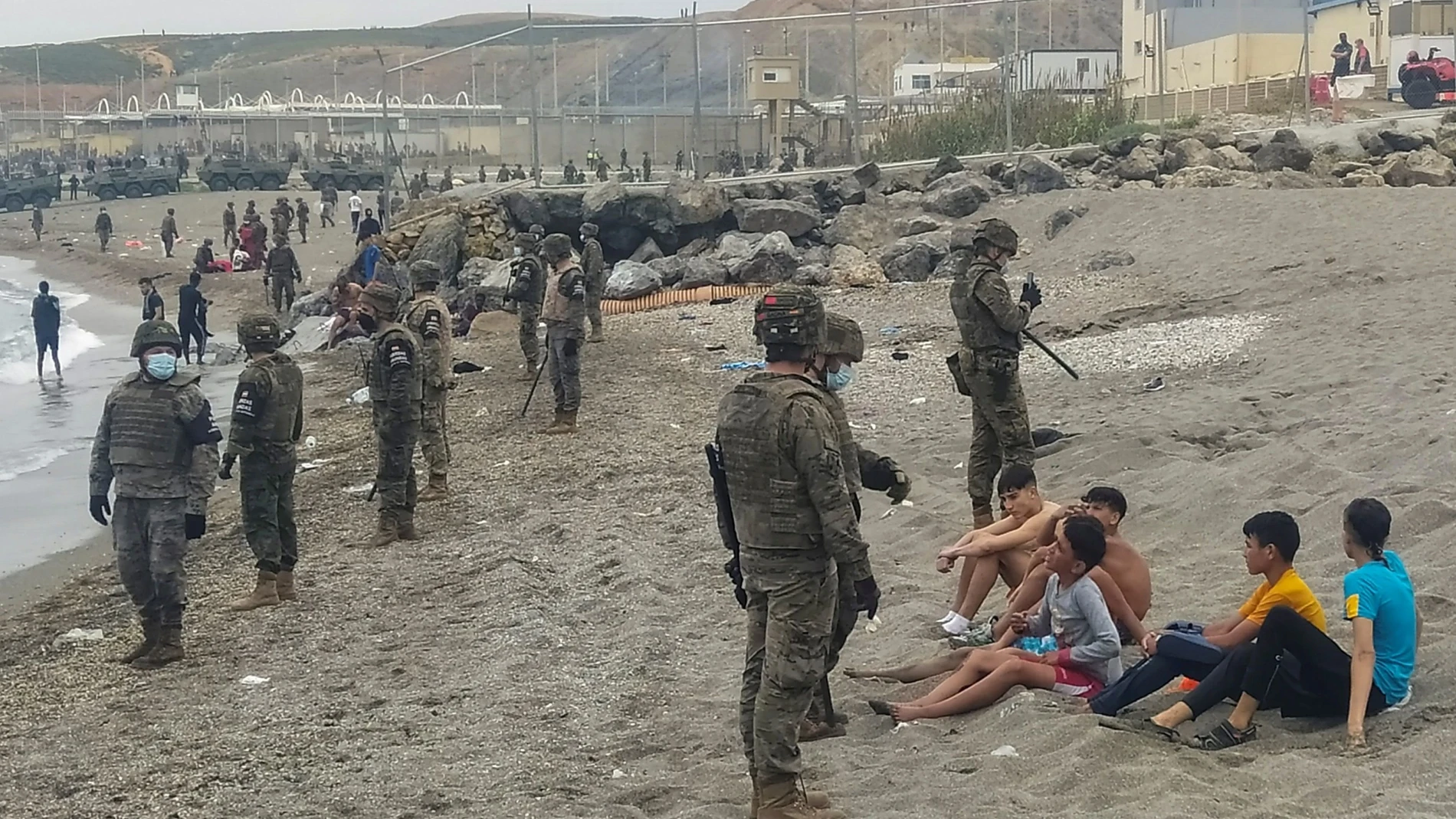 Miembros del Ejército observan a un grupo de inmigrantes que ha llegado a nado en los espigones fronterizos de Ceuta en una avalancha de inmigrantes sin precedentes en España