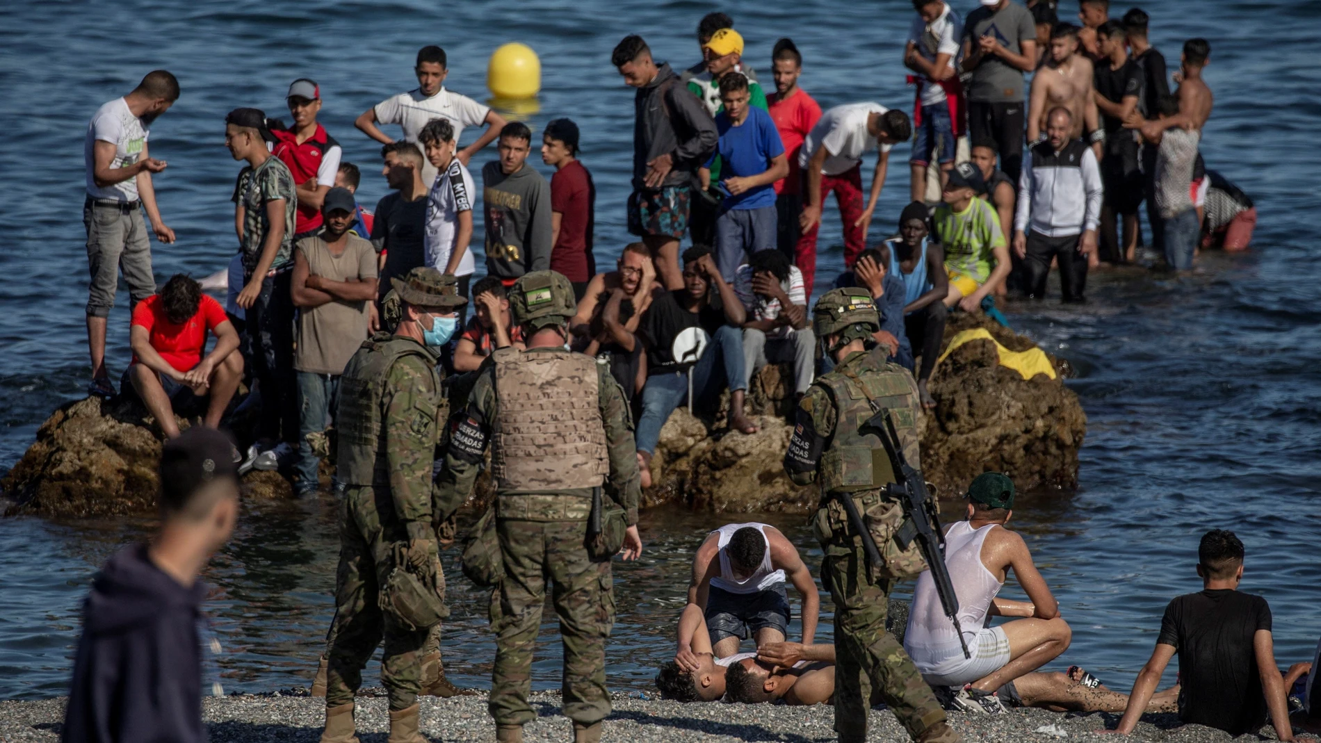 Soldados del Ejército de Tierra observan como un grupo de inmigrantes alcanzan la playa fronteriza de El Tarajal de Ceuta, este martes en una avalancha de inmigrantes sin precedentes en España al registrarse la entrada en 24 horas de 5.000 personas.
