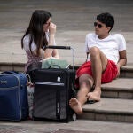 Dos turistas descansan junto a sus maletas en una plaza del centro histórico de Valencia.