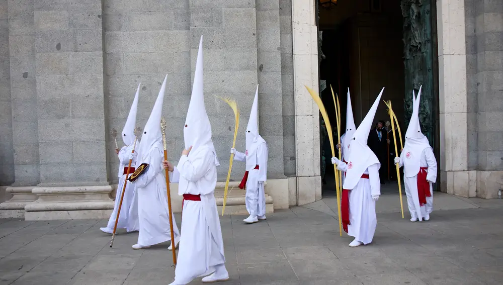 Varios nazarenos, con palmas, de la comitiva de la procesión de la Borriquita, salen de la catedral de La Almudena