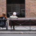 Imagen de dos personas mayores, una en silla de ruedas y la otra sentada en un banco de la calle Sagasta (Madrid)