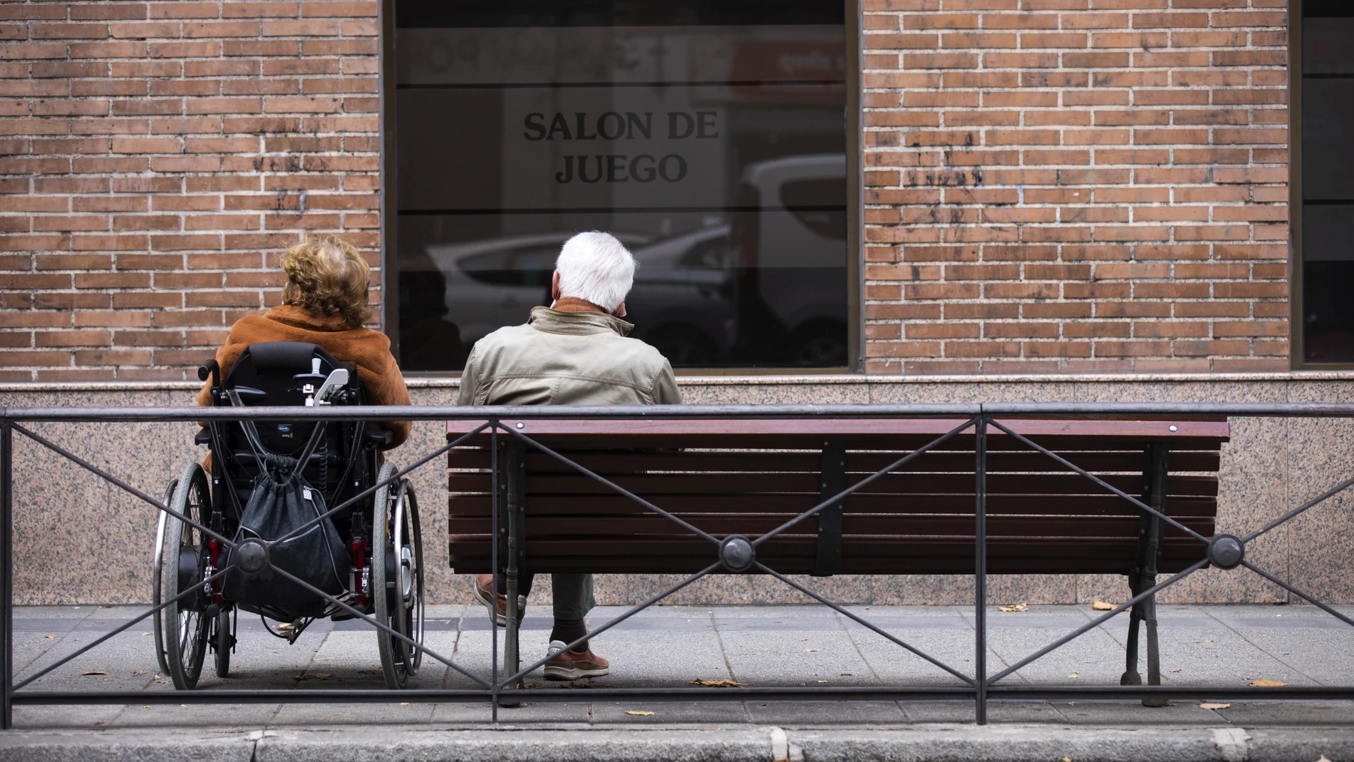 Imagen de dos personas mayores, una en silla de ruedas y la otra sentada en un banco de la calle Sagasta (Madrid)