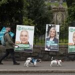 A man walks his dogs past election posters on the Falls road in West Belfast, Northern Ireland, Thursday May 5, 2022. Sinn Fein, a force in Irish republicanism on both sides of the Irish border looks likely to become the largest party in the assembly, according to polls ahead of the May 5, 2022 local elections. (AP Photo/Peter Morrison)