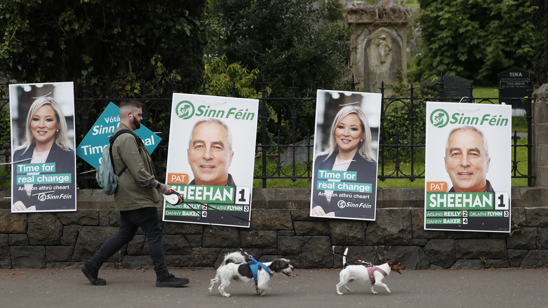 A man walks his dogs past election posters on the Falls road in West Belfast, Northern Ireland, Thursday May 5, 2022. Sinn Fein, a force in Irish republicanism on both sides of the Irish border looks likely to become the largest party in the assembly, according to polls ahead of the May 5, 2022 local elections. (AP Photo/Peter Morrison)