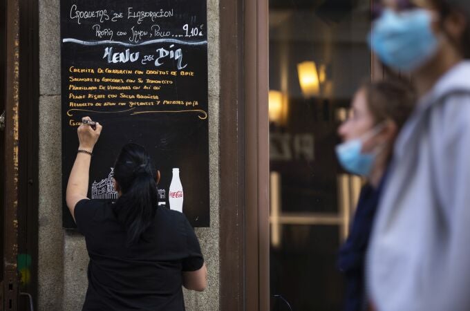 Bares y restaurantes en Madrid. Imagen de una camarera apuntando en una pizarra fuera del local el menú del día.