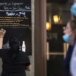 Bares y restaurantes en Madrid. Imagen de una camarera apuntando en una pizarra fuera del local el menú del día.