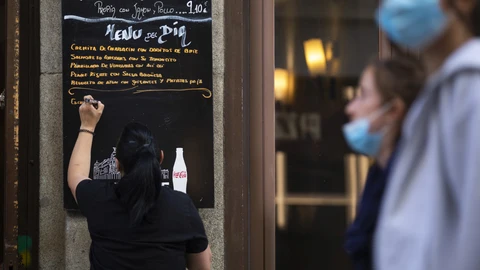 Bares y restaurantes en Madrid. Imagen de una camarera apuntando en una pizarra fuera del local el menú del día.