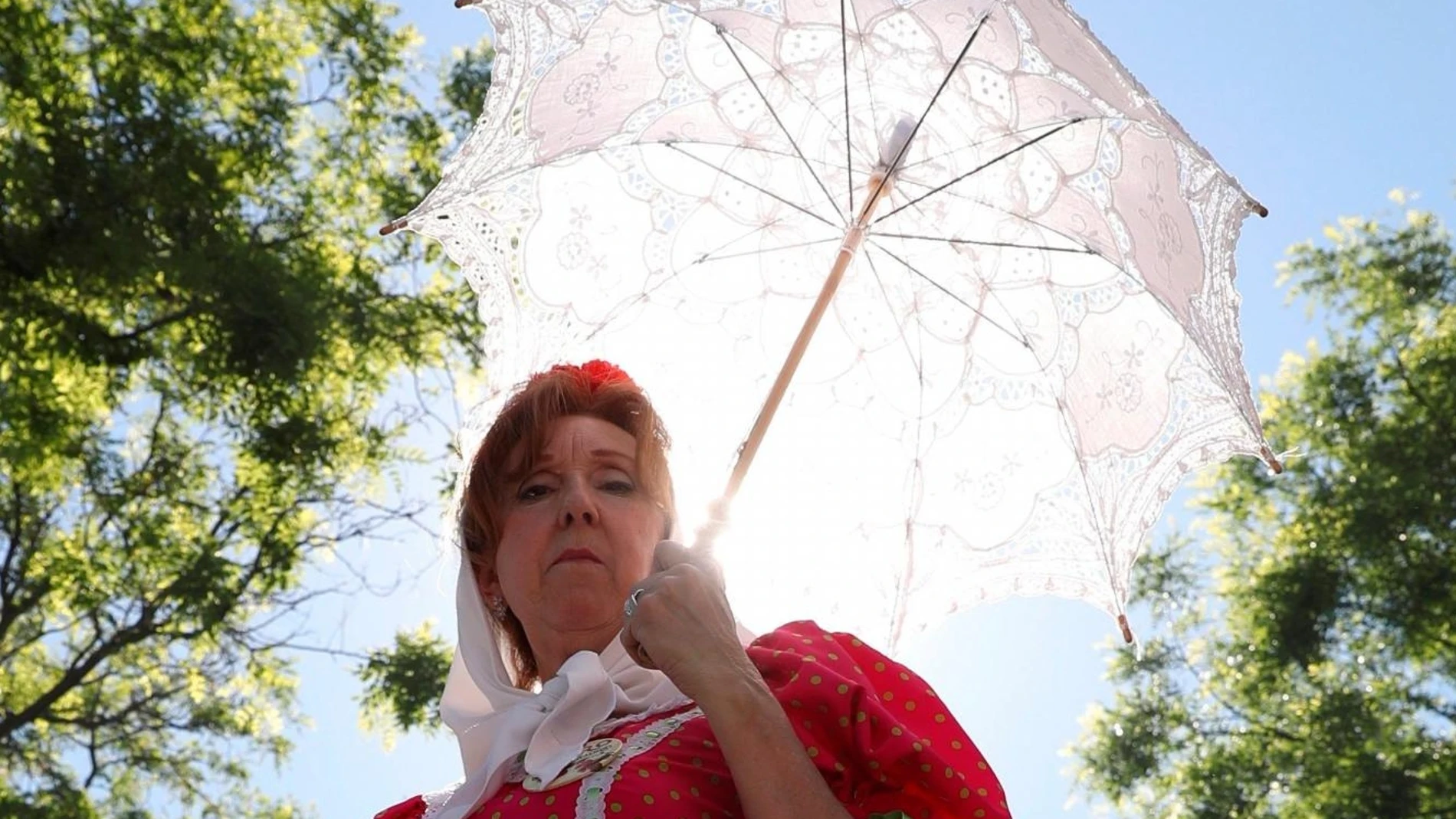 Una mujer vestida de chulapa se protege del sol con un paraguas en los alrededores de la Ermita del Santo