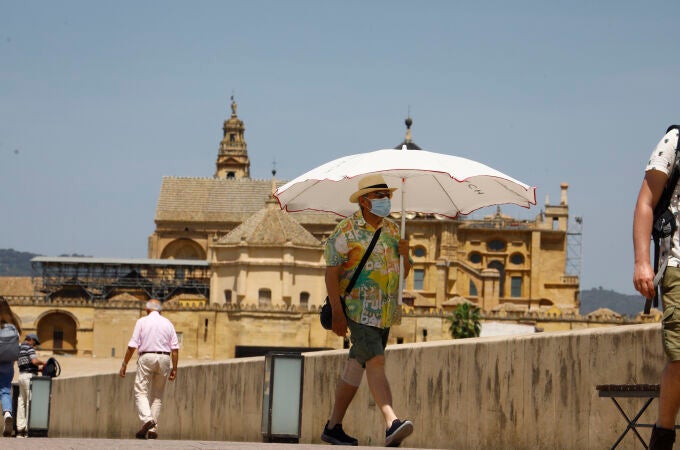 Una persona se protege con una sombrilla del intenso calor mientras pasea por el puente romano de Córdoba