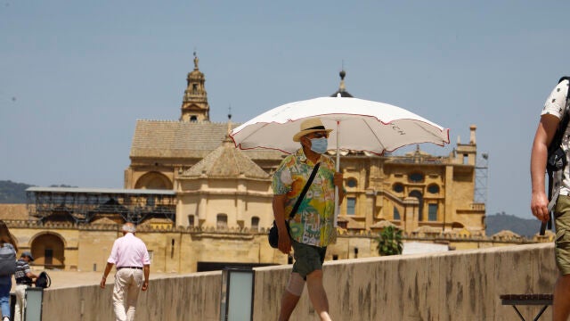 Una persona se protege con una sombrilla del intenso calor mientras pasea por el puente romano de Córdoba