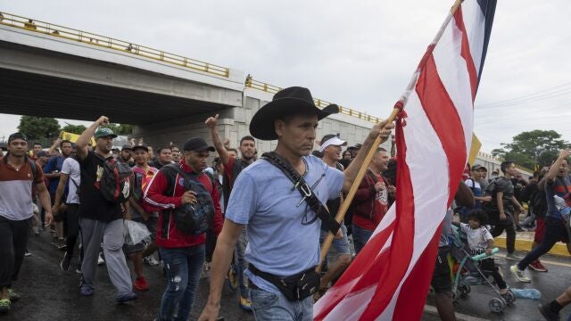 ADDS IDENTIFICATION - Roberto Marquez, a Mexican painter who lives between Mexico and the U.S., carries a U.S. flag and pulls luggage as he joins a migrant caravan leaving the city of Tapachula in Chiapas state, Mexico, early Monday, June 6, 2022. Marquez said he has accompanied other caravans since 2018, to do humanitarian work and get artistic inspiration. The migrants set out walking early Monday, tired of waiting to normalize their status in southern Mexico where there is little work. (AP Photo/Isabel Mateos)