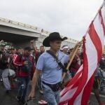 ADDS IDENTIFICATION - Roberto Marquez, a Mexican painter who lives between Mexico and the U.S., carries a U.S. flag and pulls luggage as he joins a migrant caravan leaving the city of Tapachula in Chiapas state, Mexico, early Monday, June 6, 2022. Marquez said he has accompanied other caravans since 2018, to do humanitarian work and get artistic inspiration. The migrants set out walking early Monday, tired of waiting to normalize their status in southern Mexico where there is little work. (AP Photo/Isabel Mateos)