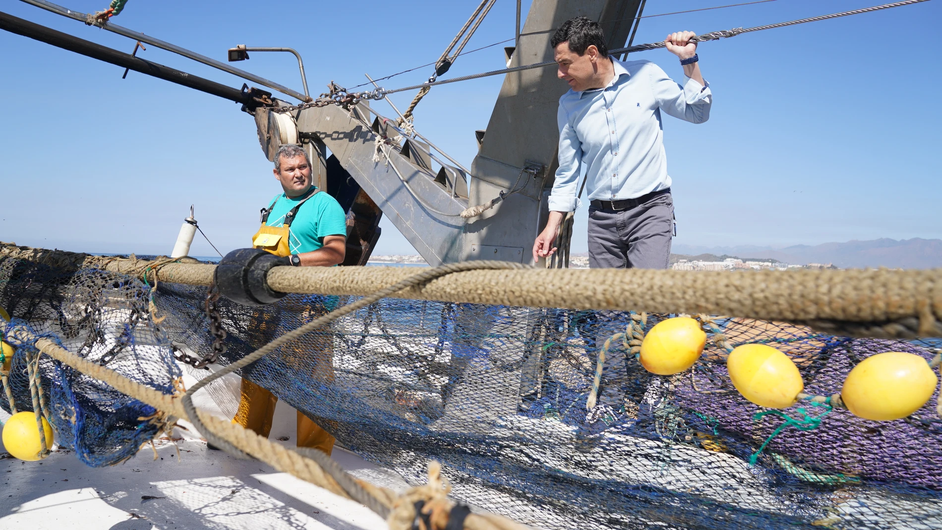 El presidente de la Junta y candidato del PP a la reelección, Juanma Moreno (d), en un barco de pesca para hablar con sus trabajadores de las faenas que realizan, en Fuengirola. EFE/PP