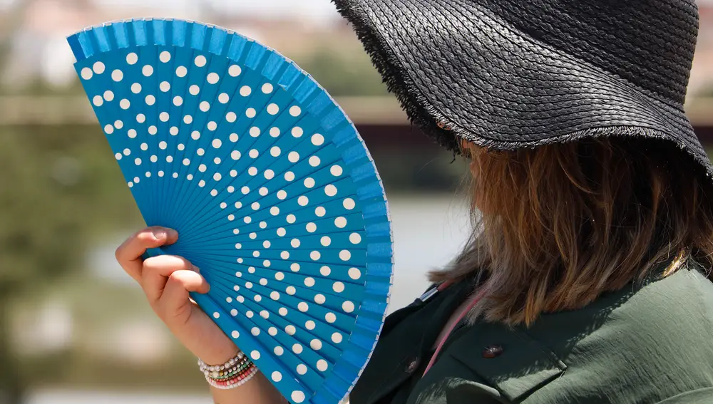 En la imagen, una mujer se protege de las altas temperaturas de la ola de calor con un sombrero y con un abanico durante esta semana en Córoba | Fuente: EFE/Salas