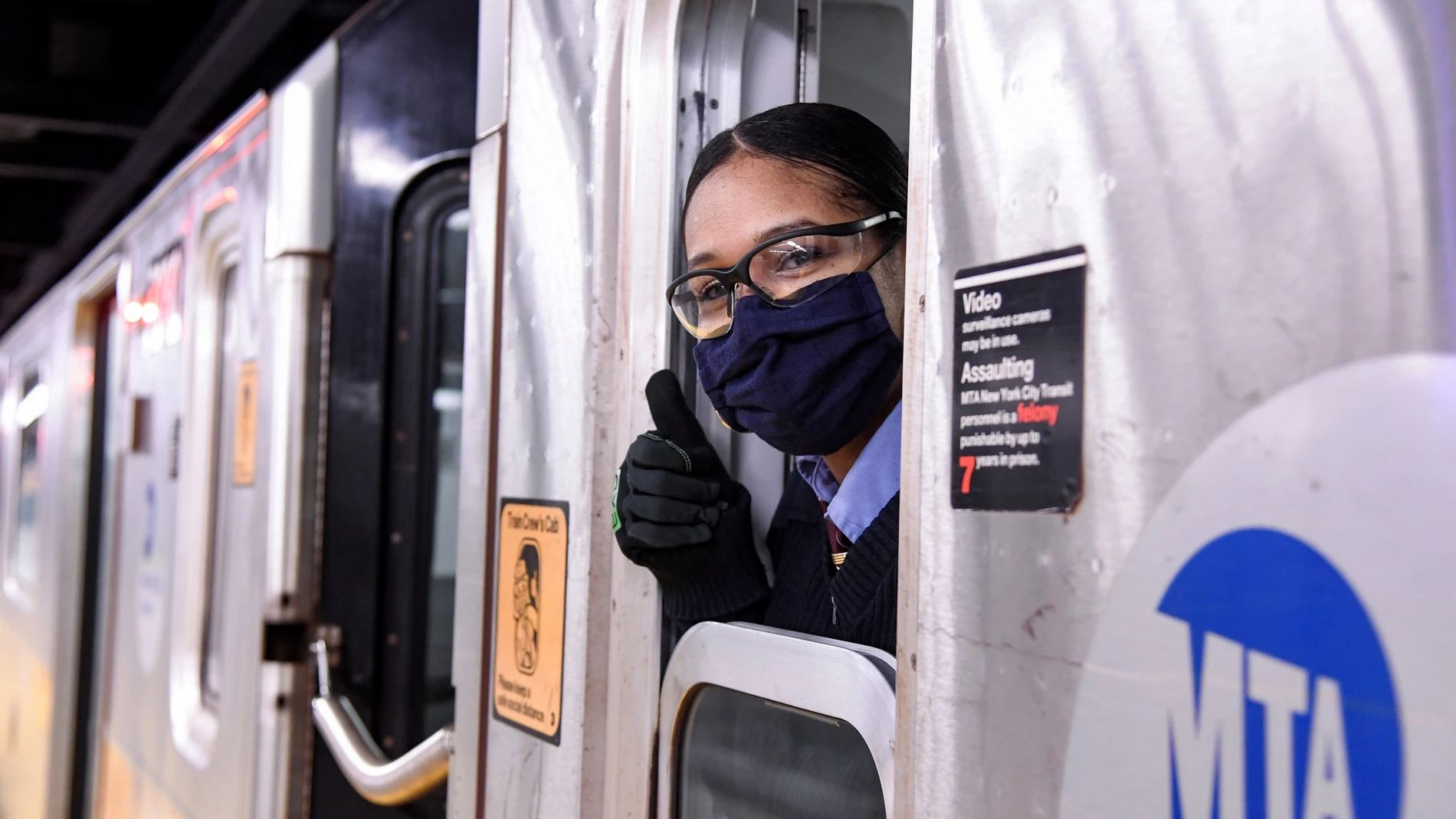 Una persona con mascarilla y gafas asomándose a la ventanilla del tren y enseñando el pulgar hacia arriba (signo de "ok")