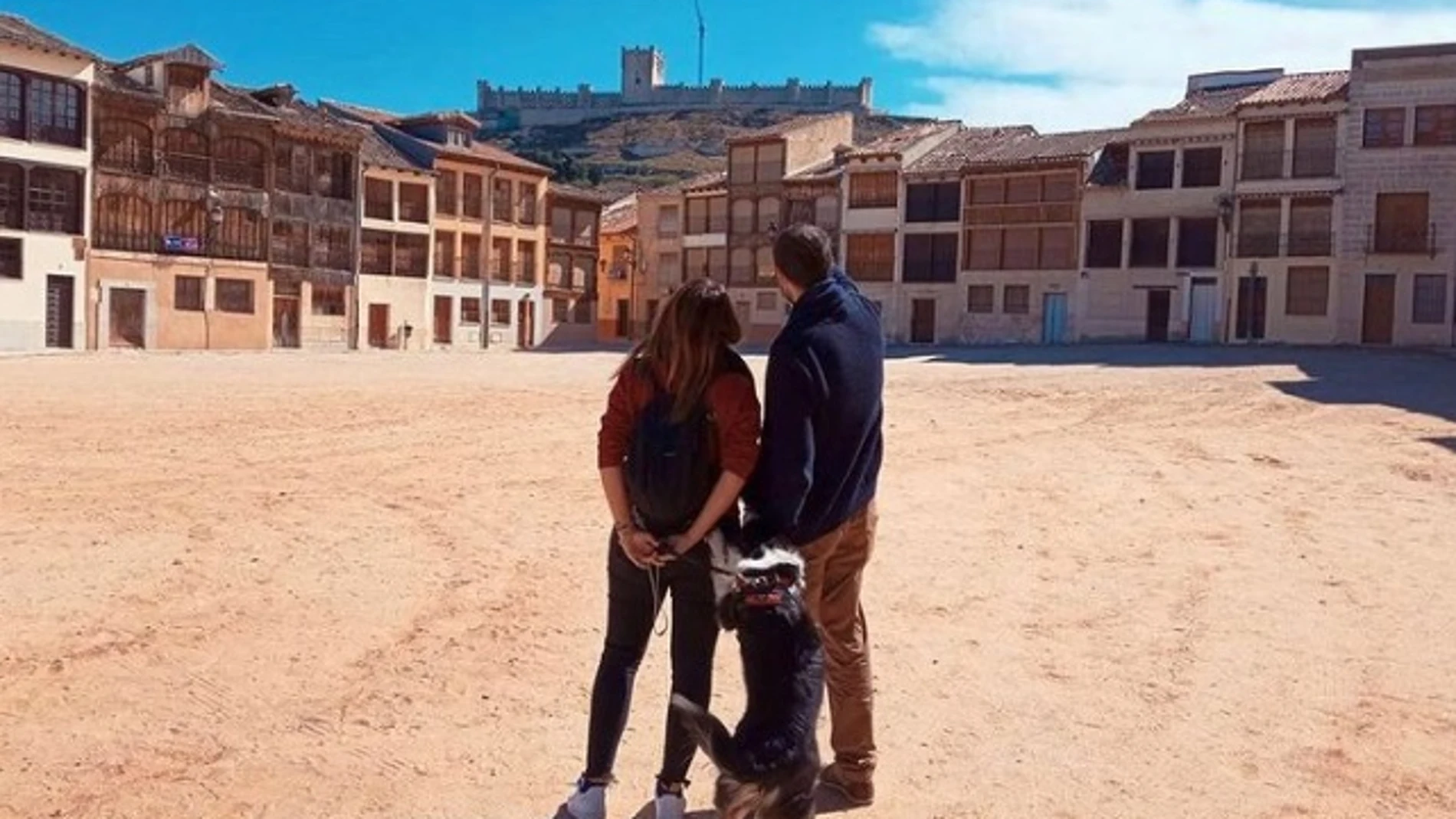 Una pareja con su perro contempla la vista del castillo de Peñafiel desde la Plaza del Coso