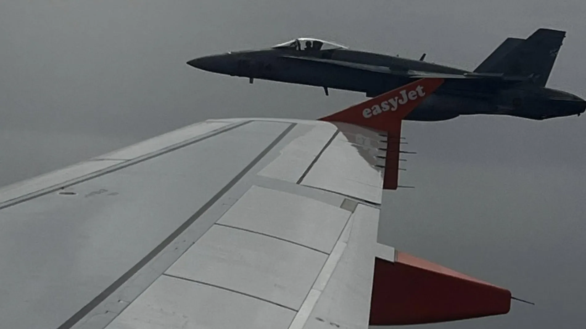 Un avión F-18 vuela cerca de las distintivas puntas de las alas naranjas del avión A-319 de EasyJet
