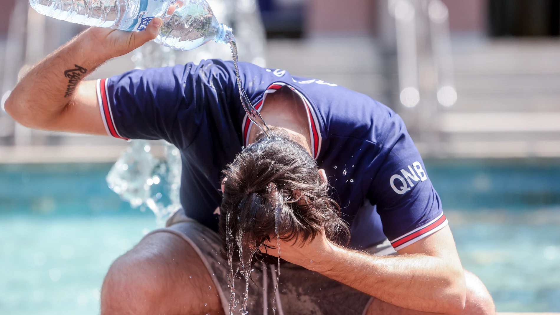 Un joven se tira una botella de agua por encima para combatir el calor