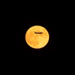 Un avión en dirección al aeropuerto del Prat pasa por delante de la luna llena