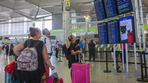 Varias personas miran los paneles informativos de los vuelos en la Terminal 3 de salidas del aeropuerto de Málaga. EFE/Álvaro Cabrera