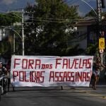 Residentes caminan sosteniendo una pancarta con un mensaje que dice en portugués: "Fuera de la favela policía asesina", luego de una operación policial que resultó en múltiples muertes, en la favela Complexo do Alemao en Río de Janeiro, Brasil, el jueves 21 de julio. 2022. (Foto AP/Silvia Izquierdo)