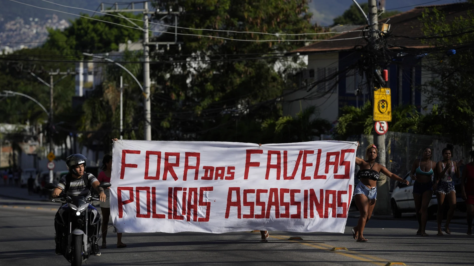 Residentes caminan sosteniendo una pancarta con un mensaje que dice en portugués: "Fuera de la favela policía asesina", luego de una operación policial que resultó en múltiples muertes, en la favela Complexo do Alemao en Río de Janeiro, Brasil, el jueves 21 de julio. 2022. (Foto AP/Silvia Izquierdo)