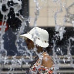 Una mujer ataviada con gorro y gafas de sol pasea junto a una fuente en Córdoba. EFE/Salas