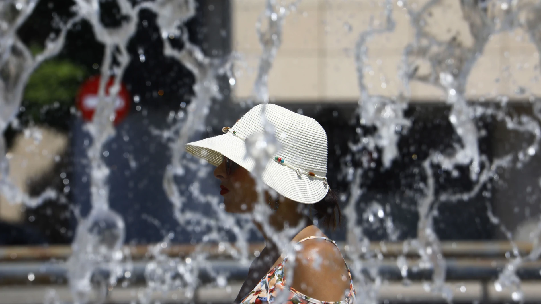 Una mujer ataviada con gorro y gafas de sol pasea junto a una fuente en Córdoba. EFE/Salas