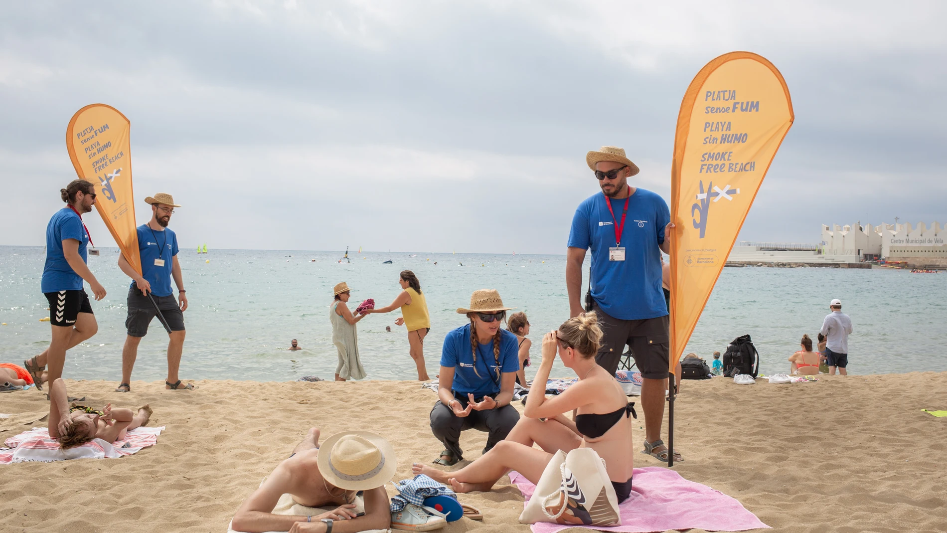Dos informadores conversan de la nueva prohibición de fumar con bañistas, en la playa del Bogatell