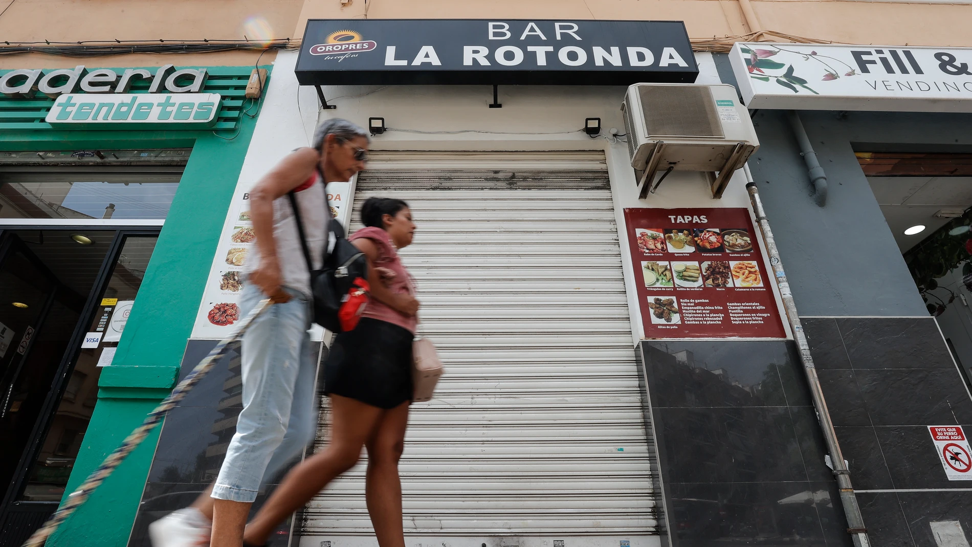 En la imagen dos mujeres pasan ante la puerta del bar donde ocurrió la agresión