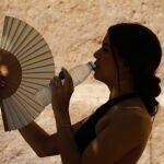 Una mujer bebe agua y se abanica mientras pasea por el barrio de la Judería de Córdoba. EFE/ Salas