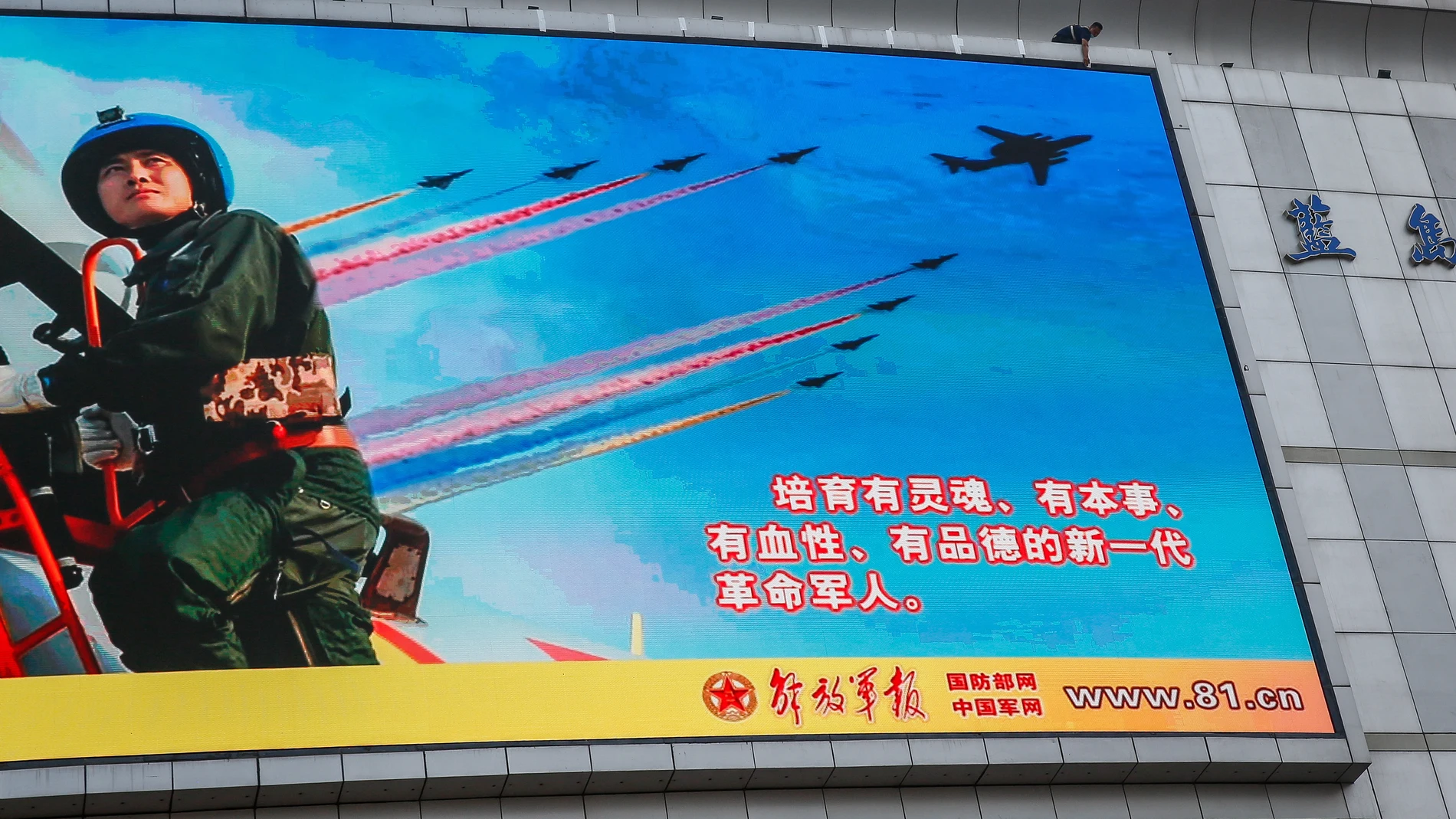 Un hombre (arriba) coloca una cinta a lo largo de un anuncio para conmemorar el 95º aniversario de la fundación del Ejército Popular de Liberación (EPL) expuesto en Pekín