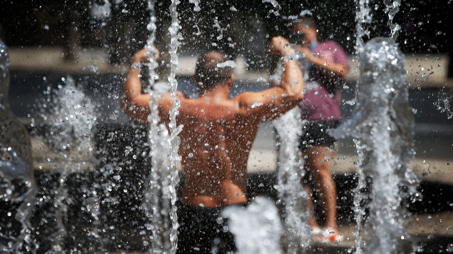 Un hombre se hace fotos mientras mitiga el calor en una fuentes de un parque de Alicante.