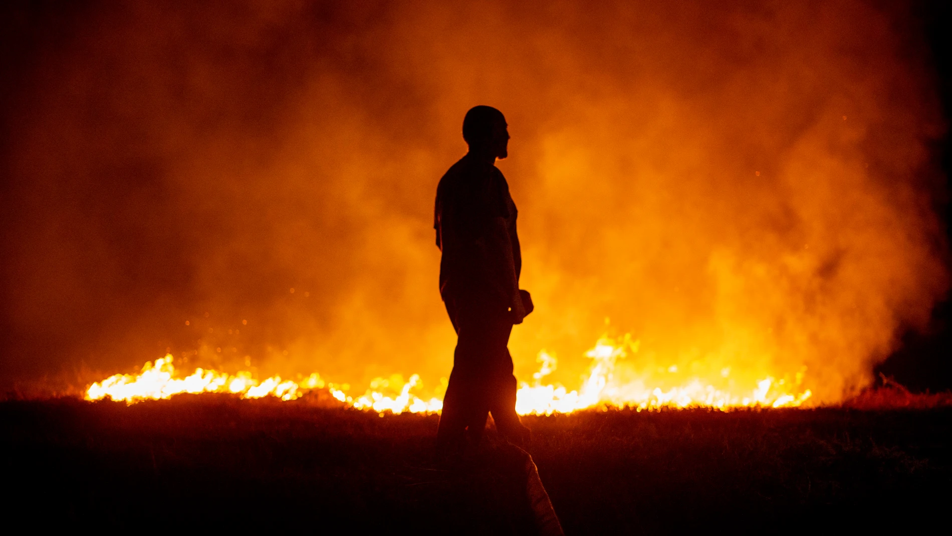 Un vecino ante las llamas mientras colabora en las labores de extinción del incendio de Cures, en Boiro, A Coruña