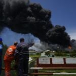 Trabajadores del Sindicato Petrolero de Cuba (CUPET) observan una enorme columna de humo que se eleva desde la Base de Superpetroleros de Matanzas, mientras los bomberos trabajan para sofocar un incendio que comenzó durante una tormenta eléctrica la noche anterior