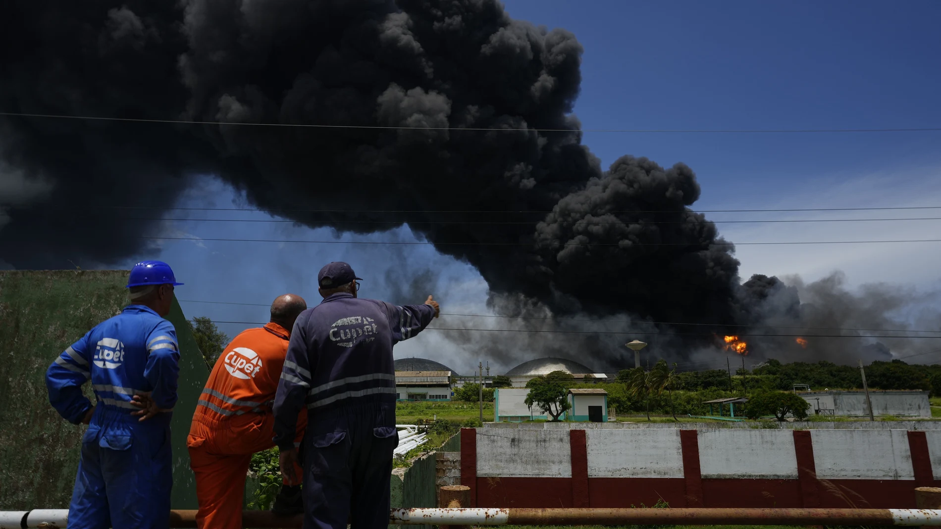 Trabajadores del Sindicato Petrolero de Cuba (CUPET) observan una enorme columna de humo que se eleva desde la Base de Superpetroleros de Matanzas, mientras los bomberos trabajan para sofocar un incendio que comenzó durante una tormenta eléctrica la noche anterior