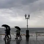 Varias personas se protegen con el paraguas de la lluvia, en el paseo de muro de la playa de San Lorenzo de Gijón