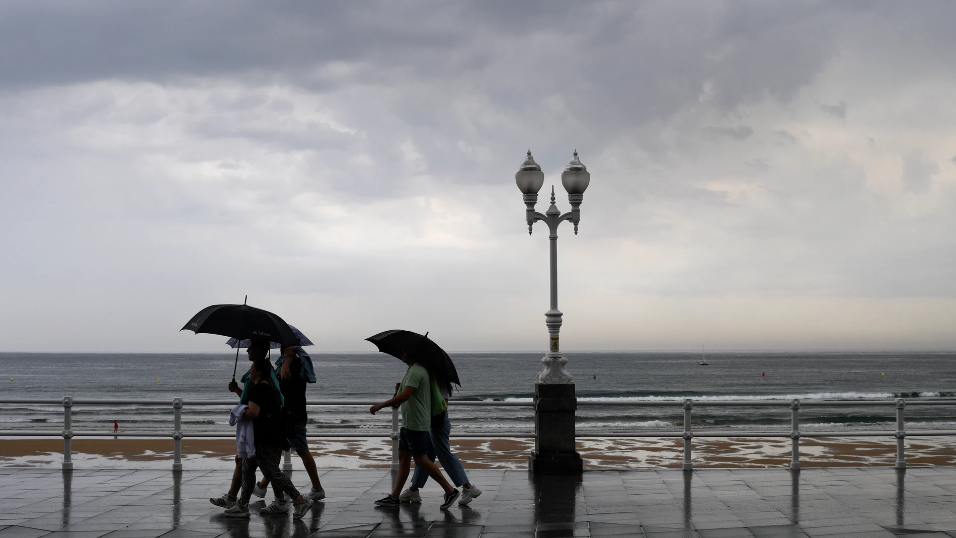 Varias personas se protegen con el paraguas de la lluvia, en el paseo de muro de la playa de San Lorenzo de Gijón