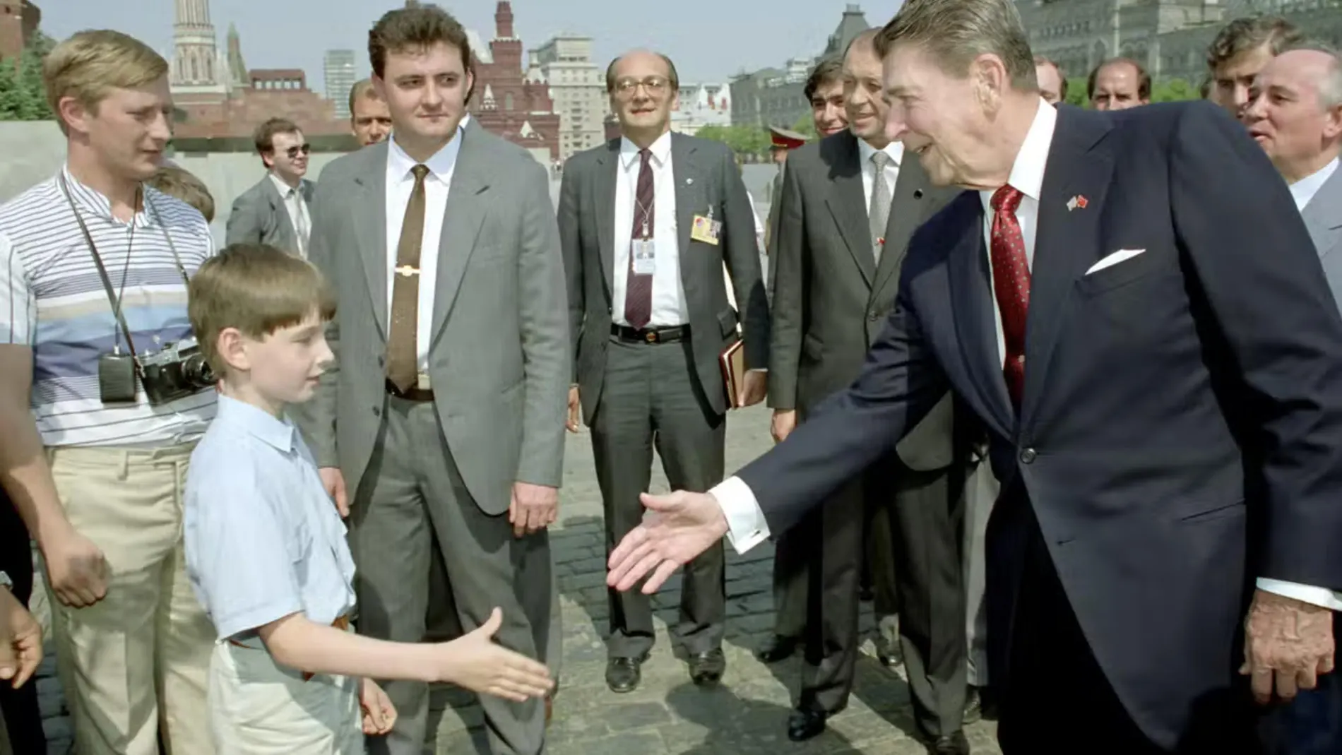 Ronald Reagan le da la mano a un niño mientras Mijaíl Gorbachov (der.) observa y el joven rubio (izq.) podría ser Vladimir Putin (izq.) espiando al presidente de EE UU