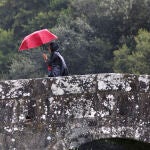 Una mujer pasa esta mañana por el puente de Sar en Santiago de Compostela, en donde una borrasca afecta a toda la comunidad gallega con un frente frío y lluvias.