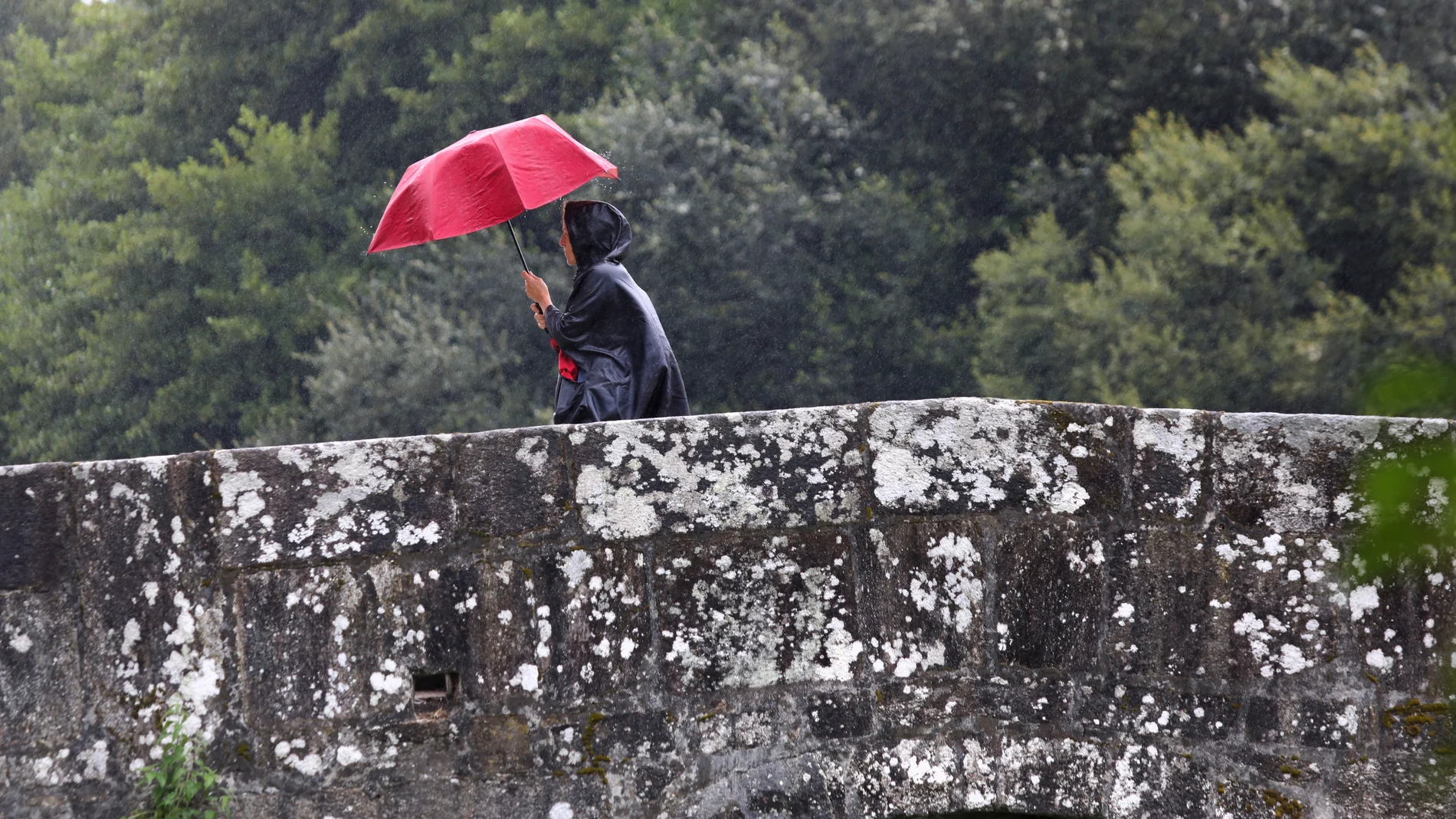 Una mujer pasa esta mañana por el puente de Sar en Santiago de Compostela, en donde una borrasca afecta a toda la comunidad gallega con un frente frío y lluvias.