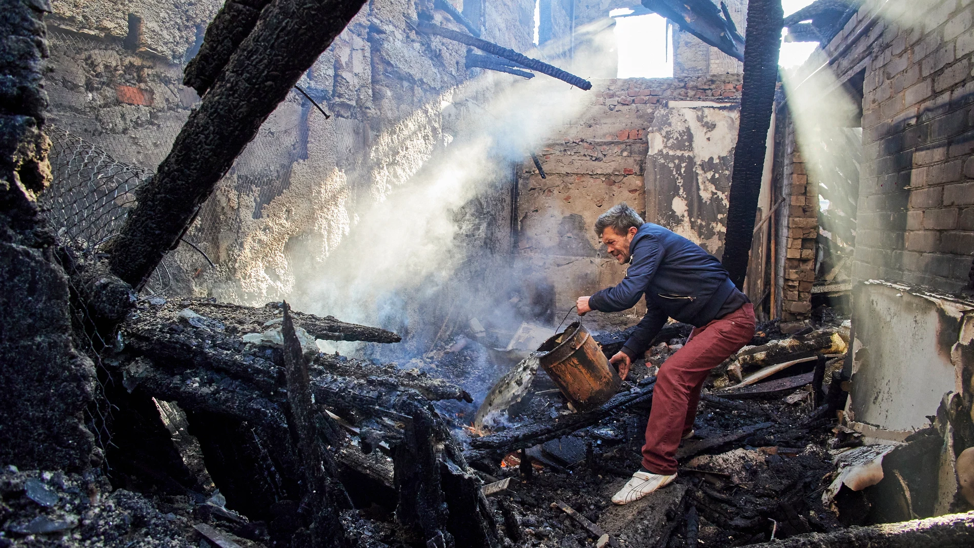 Un vecino trata de apagar un incendio en un edificio destruido en Jarkov, la segunda mayor de Ucrania