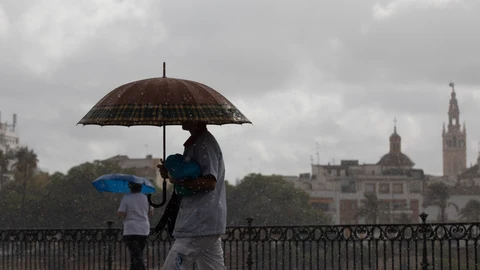Dos personas caminan bajo sus paraguas en Sevilla