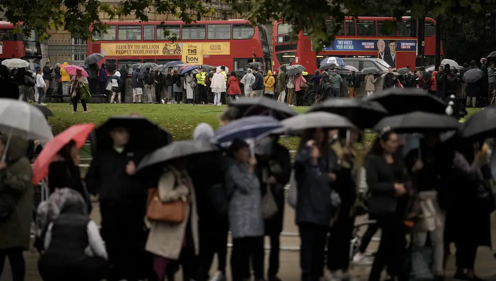 La gente hace cola en las calles esperando a que el coche fúnebre de Estado que lleva el féretro de la reina Isabel II pase de camino al Palacio de Buckingham en Londres