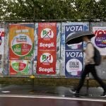 Un hombre pasea bajo el paraguas en una calle de Milán con carteles electorales de los partidos que se presentan a las elecciones del domingo