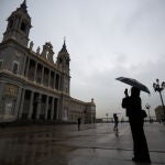 Una mujer se protege de la lluvia con un paraguas mientras hace una foto de la fachada de la catedral de La Almudena, en Madrid