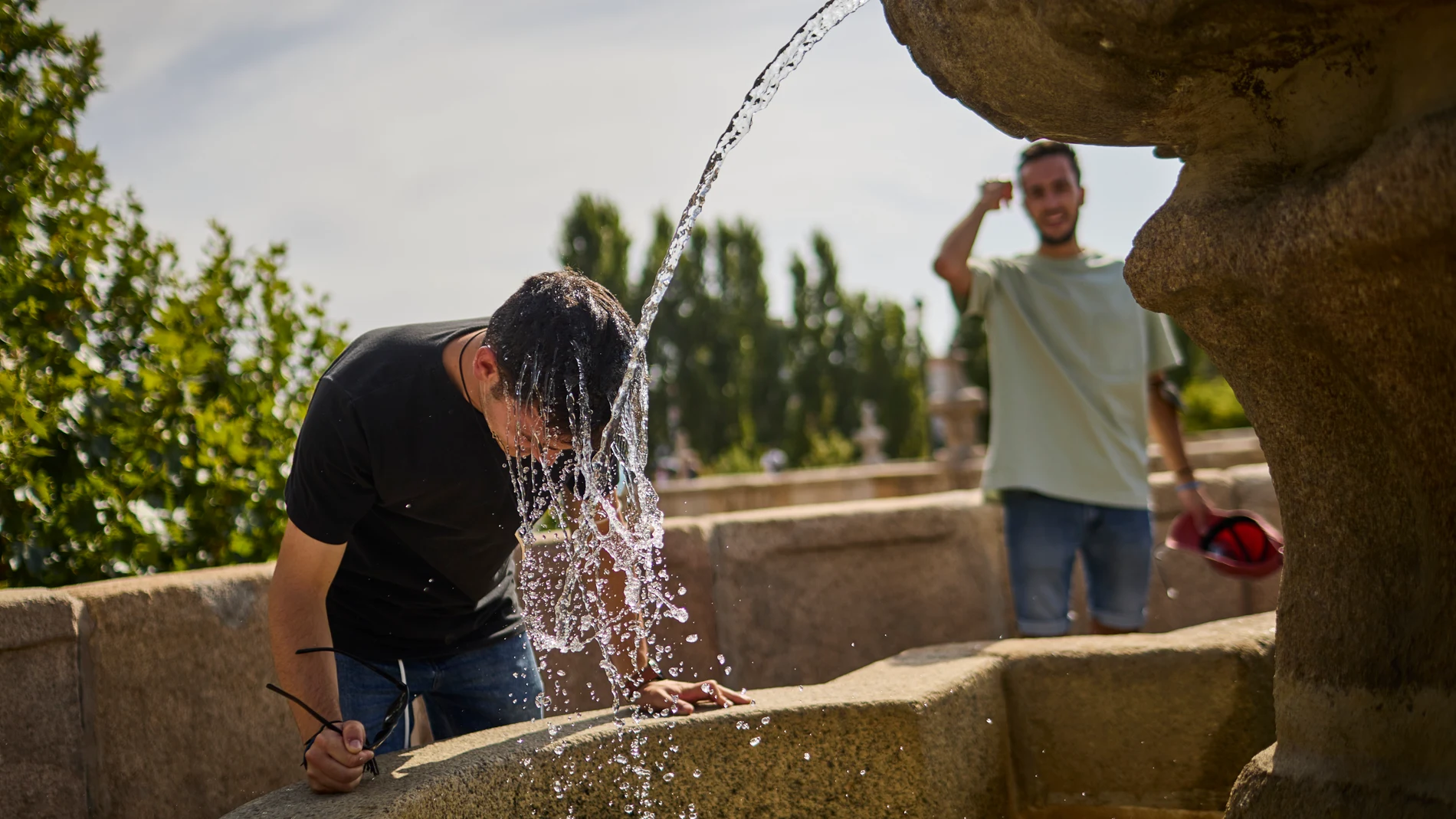 Personas intentan refrescarse en una fuente para combatir el calor en Madrid