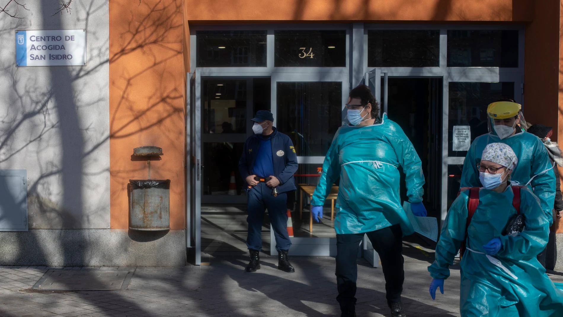 Un empleado de seguridad vigila una de las puertas por donde salen trabajadores sanitarios totalmente protegidos del centro de acogida San Isidro, en Madrid