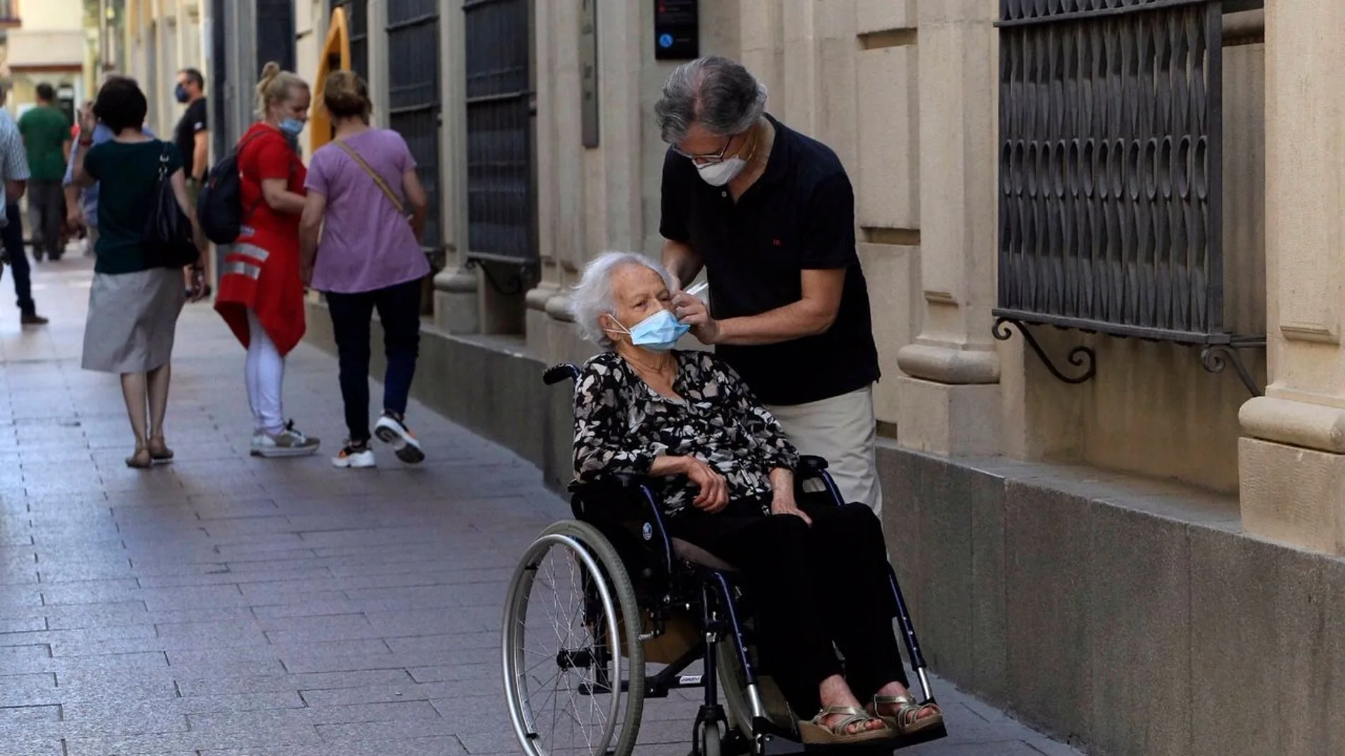 Un hombre ayuda a una mujer en silla de ruedas a colocarse la mascarilla