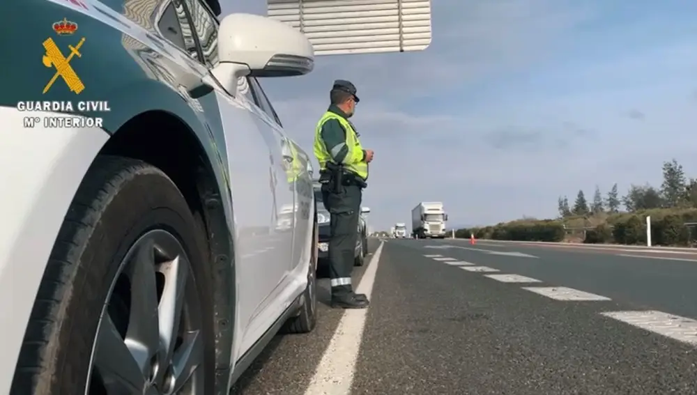 Un agente de la Guardia Civil junto a su coche en una carretera.